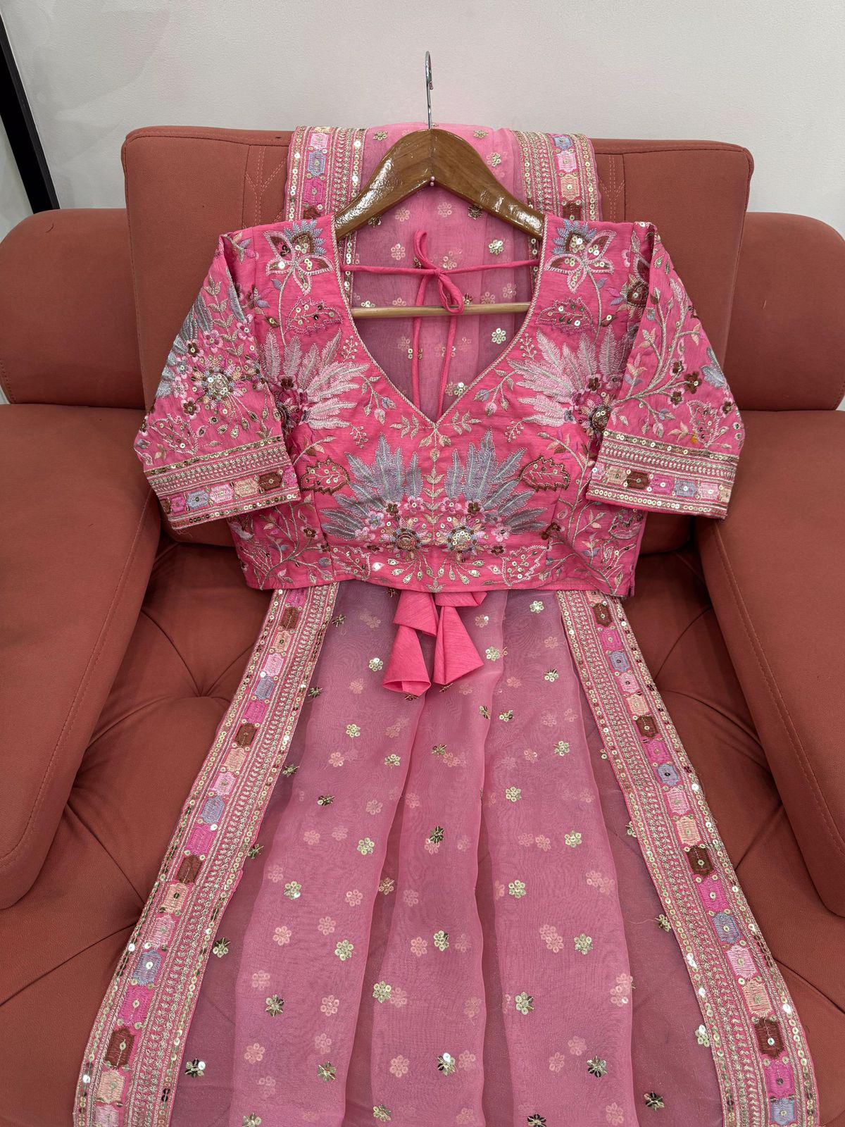 Pink embroidered traditional outfit on a hanger against a red sofa.
